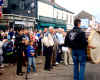 Crowd, including Korean visitor, watch Lambegs depart.